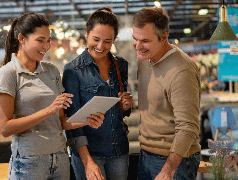Three people examining a tablet together in a retail store, engaged in discussion about its features.