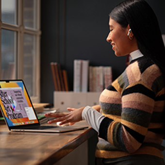 A woman seated at a desk, focused on her laptop while working in a well-lit office environment.