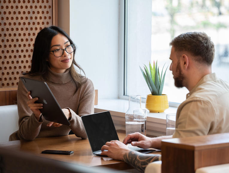 A man and woman collaborate at a table with a laptop, discussing their work and sharing insights.